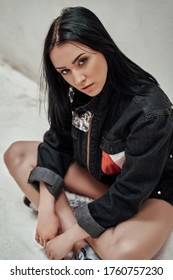Cool And Daring Young Woman Sitting On The Studio Floor, Looking Thoughtful And Wearing Sporty Clothes