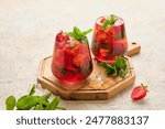 Cool drink, ice tea with strawberries and mint in glasses on a wooden board on a light concrete background. Summer drinks. Soft drinks