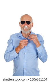 Cool elderly man having fun with photo booth accessories. Holding black sunglasses and mustache on isolated background