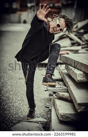 A cool extraordinary mature man with dreadlocks and tattoos in black clothes with ethnic ornaments poses expressively on the backstreet. Rock and punk culture. 