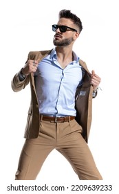 Cool Fashion Businessman With Open Collar Shirt And Sunglasses Holding And Opening Brown Suit And Looking To Side In Front Of White Background In Studio