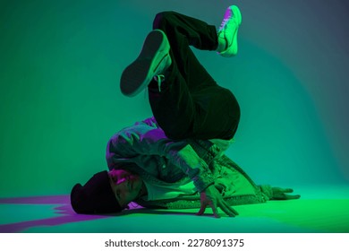 Cool fashion stylish hipster professional b-boy dancer in jeans clothes with denim jacket and sneakers dancing on the floor in a creative studio with purple and green light - Shutterstock ID 2278091375