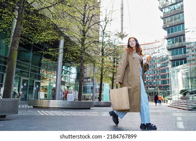 Cool Fashion Stylish Teen Girl Model Shopper Buyer Wearing Trench Coat Holding Paper Shopping Bags Walking On Busy Big City Street Buying Sale Retail Clothes In Downtown Store Mall Outdoors.