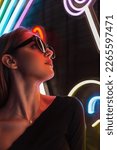 Cool fashionable urban portrait of a pretty stylish girl in black clothes with stylish sunglasses on a dark background with colorful neon lights