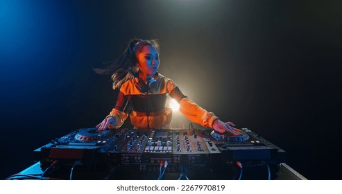 Cool female asian dj is working in a nightclub, standing at turntables, creating a dance music set - nightlife concept  - Shutterstock ID 2267970819