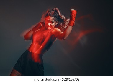 Cool female fighter in boxing bandages trains in studio in red neon light. Mixed martial arts. Long exposure shot