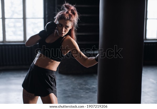 cool female fighter in boxing gloves trains in the\
gym. Mixed martial arts