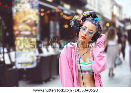 Cool funky young woman with trendy eyeglasses listening music on headphones outdoor - hipster girl with sunglasses and piercings enjoy music vibes – street fashion look with girl teen with crazy hair