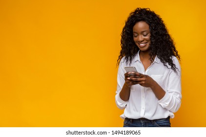 Cool Gadget And Application. Interested Black Woman Using Smartphone On Yellow Background, Copy Space