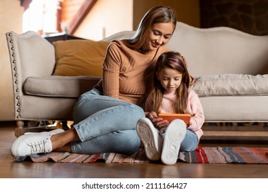 Cool Gadget And Application. Portrait Of Young Smiling Woman And Little Girl Using Mobile Phone, Sitting On The Floor Leaning On Sofa In Living Room. Family Browsing Internet, Surfing Web Together