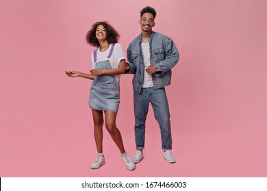 Cool Girl And Guy In Jeans Smiling And Dancing On Pink Background. Woman With Wavy Hair And Handsome Man In Denim Jacket Move On Isolated