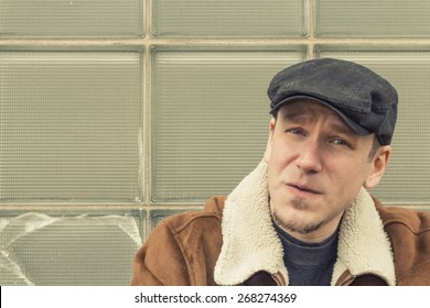 Cool Guy In Aviator Jacket And Newsie Cap Relaxes Against A Glass Wall