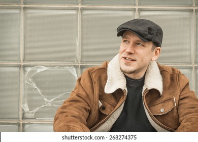 Cool Guy In Aviator Jacket And Newsie Cap Relaxes Against A Glass Wall