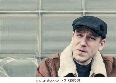 Cool Guy In Aviator Jacket And Newsie Cap Relaxes Against A Glass Wall