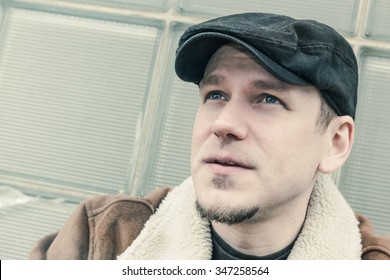 Cool Guy In Aviator Jacket And Newsie Cap Relaxes Against A Glass Wall