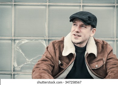 Cool Guy In Aviator Jacket And Newsie Cap Relaxes Against A Glass Wall