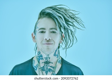 Cool handsome punk rock musician with dreadlocks and tattoos poses on a blue background joyfully smiling. Youth alternative culture.