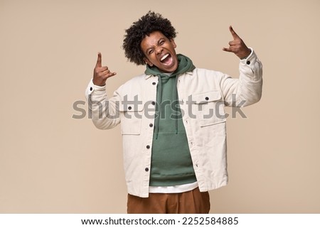 Cool happy hipster African American teen guy showing rock n roll hand sign having fun isolated on beige background. Crazy funky ethnic generation z teenager fashion model screaming having fun.