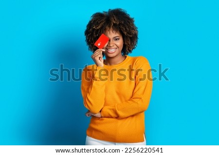 Cool happy smiling stylish attractive african american millennial lady cover one eye with red credit card, isolated on blue studio background. Unlimited shopping, e-commerce, retail, online banking