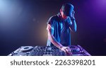 Cool hipster disc jockey performing in a nightclub at a mixer controller, spotted by colorful lights on smoked black background - nightlife concept 