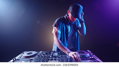 Cool hipster disc jockey performing in a nightclub at a mixer controller, spotted by colorful lights on smoked black background - nightlife concept  - Shutterstock ID 2263398201