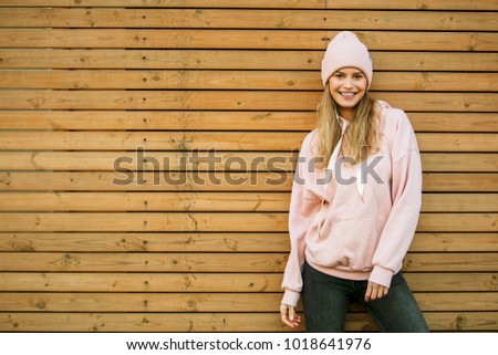 cool hipster woman happy, with smile and good energy, enjoying youth and standing on wooden wall, playing and waiting for something outside