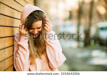 cool hipster young girl in pink hoodie standing against a wooden wall on the street enjoying youth and being happy

