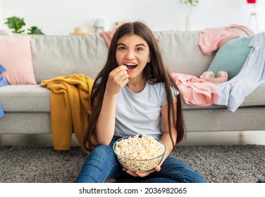 Cool Indian Teen Girl Spending Her Free Time Watching TV And Eating Popcorn On Floor At Home. Lovely Adolescent With Yummy Snack Enjoying Interesting Movie In Living Room