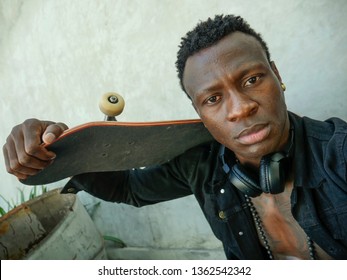 Cool Isolated Portrait Of Young Attractive And Confident Hipster Black African American Man Leaning On Street Wall Holding Skate Board As Badass Guy In Urban Style Concept