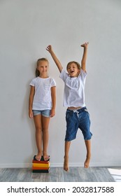 Cool Kids, Little Boy And Girl Measure Their Height And Compare, Have Fun Near White Wall