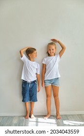 Cool kids, little boy and girl measure their height and compare, have fun near white wall