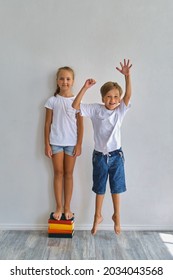 Cool Kids, Little Boy And Girl Measure Their Height And Compare, Have Fun Near White Wall