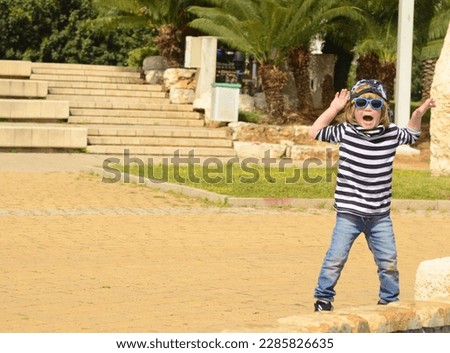Cool little boy in a striped t-shirt and sunglasses. A 4-year-old boy runs and dances in the park. Active positive boy. Good mood, summer.