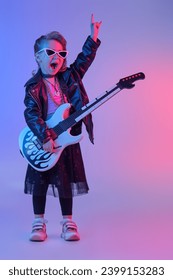 Cool little girl - rock star, rock musician. Full length portrait of a pretty girl in black clothes and a black leather jacket playing the electric guitar in the studio.