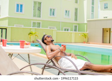 Cool Looking Black Dude Chilling By The Pool Side With A Drink In Hand, Wearing Sunglasses