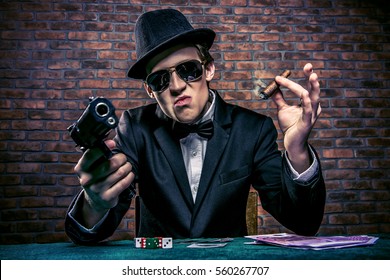 Cool Mafia Gangster mit einer Pistole sitzend auf einem Spieltisch in einem Casino. Glücksspiel, Spielkarten und Roulette.