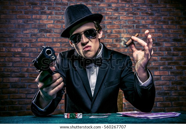 Cool mafia gangster\
with a gun sitting at a game table in a casino. Gambling, playing\
cards and roulette.