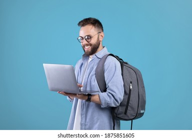Cool millennial guy with backpack using laptop for online work or studies over blue studio background. Happy young man communicating on web, watching movie, browsing internet - Shutterstock ID 1875851605