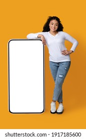 Cool Mobile App. Cheerful Black Woman Leaning At Big Smartphone With Blank White Screen, Demonstrating Copy Space For Your Design Or Advertisement, Standing Over Yellow Background, Mockup Image