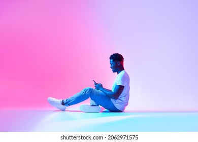 Cool Mobile App. Side View Of Happy Black Man Using Modern Smartphone In Neon Light, Copy Space. Positive African American Guy Working Or Studying Online, Browsing Social Network, Chatting On Web