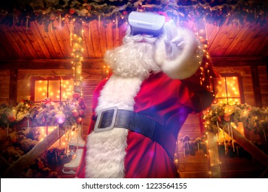 Cool Modern Santa Claus In Virtual Reality Glasses Standing Near His Decorated House. Computer Games. Christmas And New Year Concept.