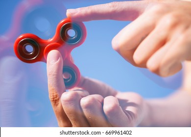 Cool new fidget spinner toy.Woman play with modern spinning device.Enjoy playing with this super trendy gadget with rotating bearing in the middle.Bright blue sky background