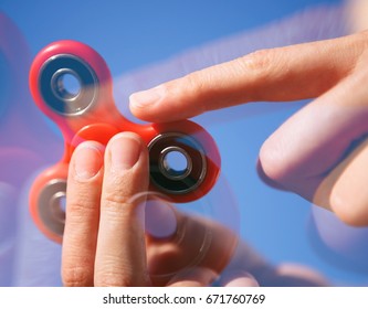 Cool new fidget spinner toy.Woman play with modern spinning device.Enjoy playing with this super trendy gadget with rotating bearing in the middle.Bright blue sky background