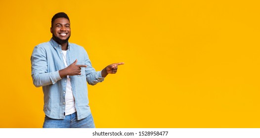 Cool offer. Cheerful african american man pointing two fingers aside at copy space on yellow studio background, panorama