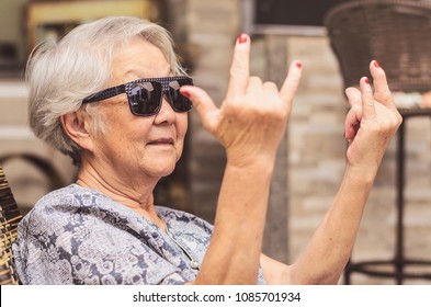 Cool old lady, wearing sunglasses doing the rock sign.