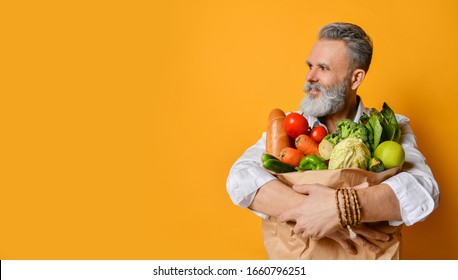 Cool old mature senior man with gray beard shopping hold grocery shopping bag with healthy organic vegetables on yellow background - Powered by Shutterstock