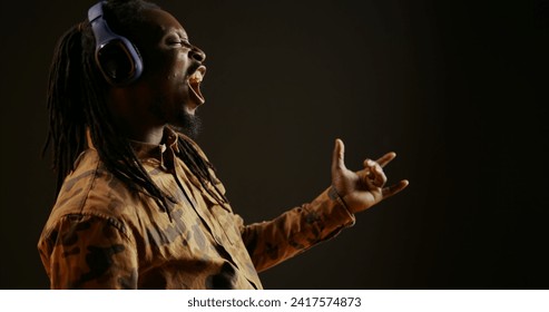 Cool person playing air guitar and listening to music on camera, pretending to play imaginary instrument and create tunes. African american man having fun with songs on headset, musical activity. - Powered by Shutterstock