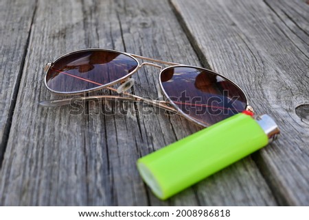 Cool pilot sun glasses isolated on a wooden table with a green lighter for smoking