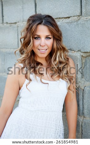 Cool pretty woman with white dress and a beautiful smile resting on a gray wall