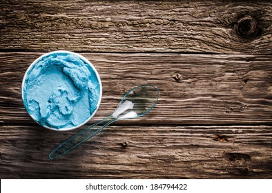 Cool Refreshing Blue Italian Ice Cream In A Takeaway Tub With A Plastic Spoon For A Welcome Treat On A Hot Summer Day Served On An Old Wooden Table With Copyspace, View From Above